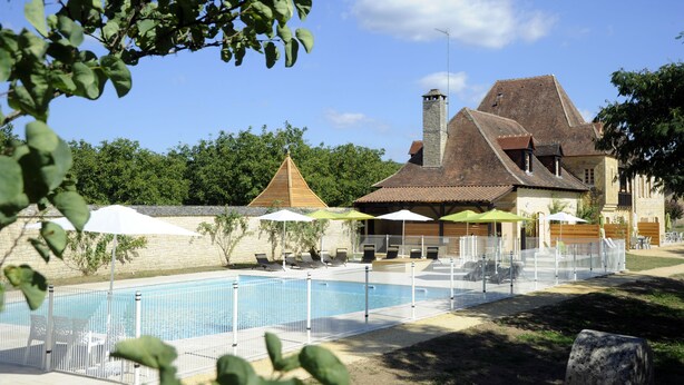 Una piscina con area recintata, sdraio e ombrelloni.