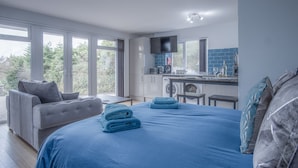 Un dormitorio con una cama grande, un sofá gris y vistas al exterior.