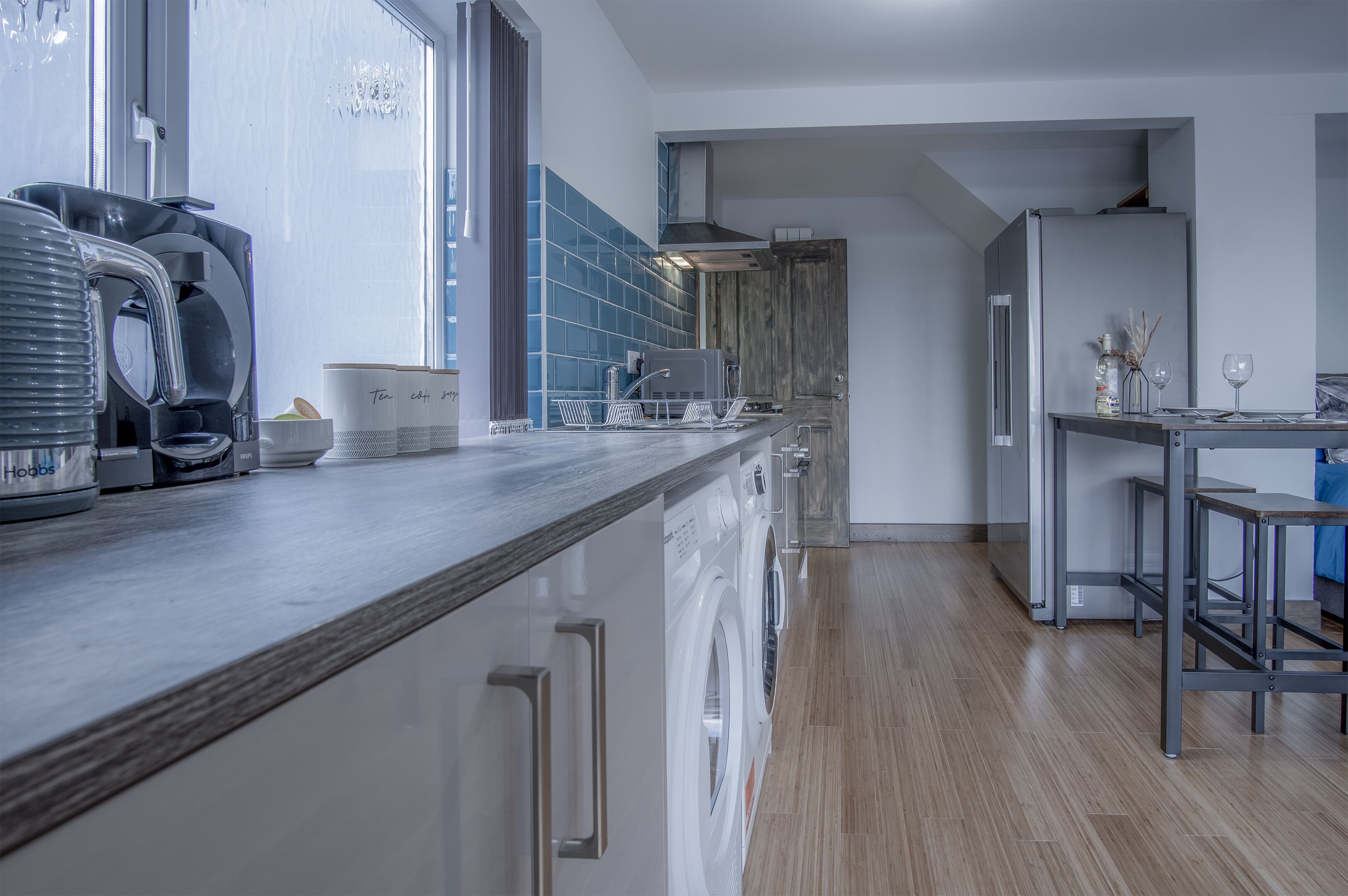 A modern kitchen with a built-in washing machine, a coffee maker, and a dining area with a table and chairs.