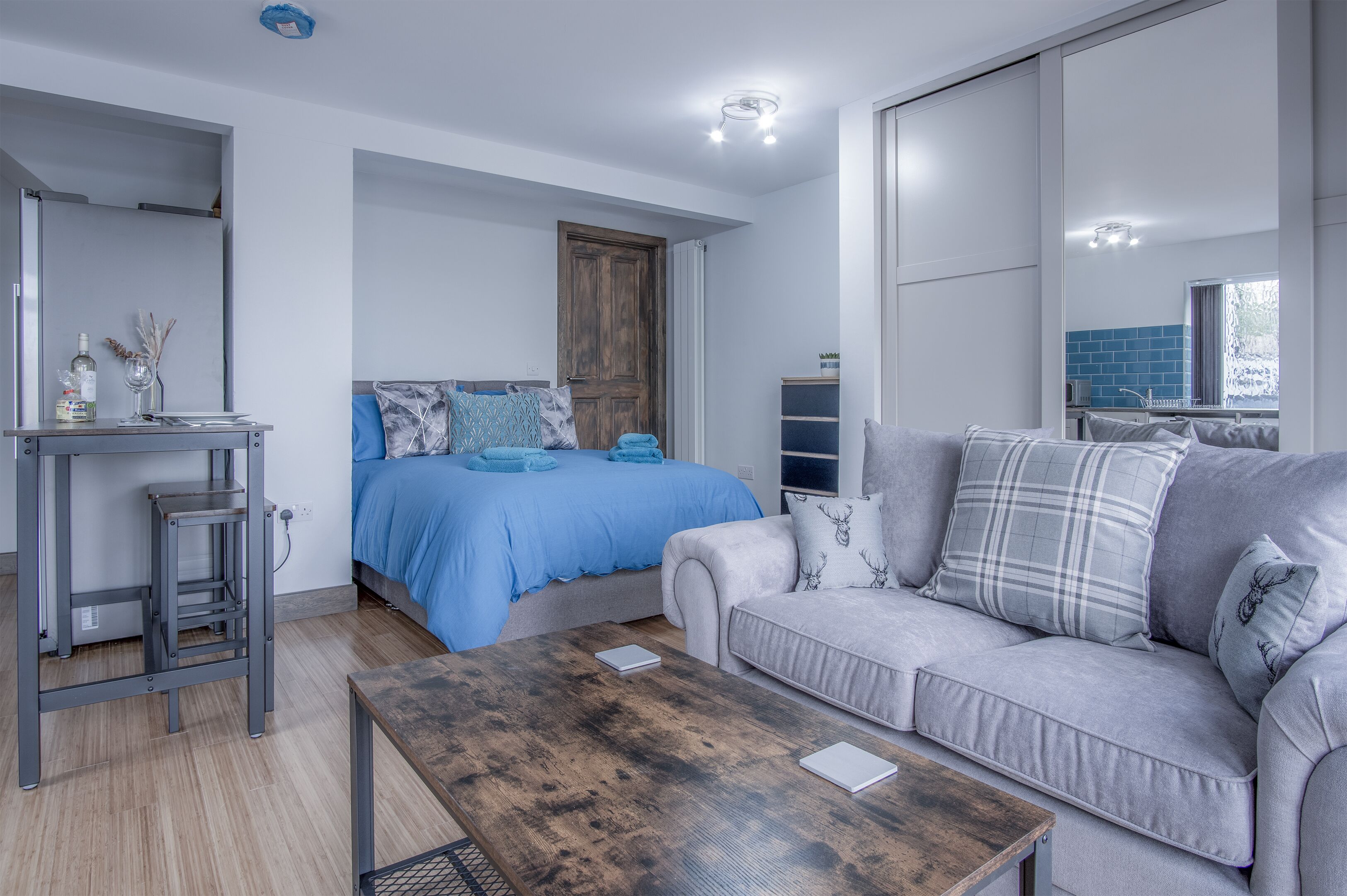 Un dormitorio moderno con una cama, un sofá, una mesa de centro de madera y un escritorio con lámpara.