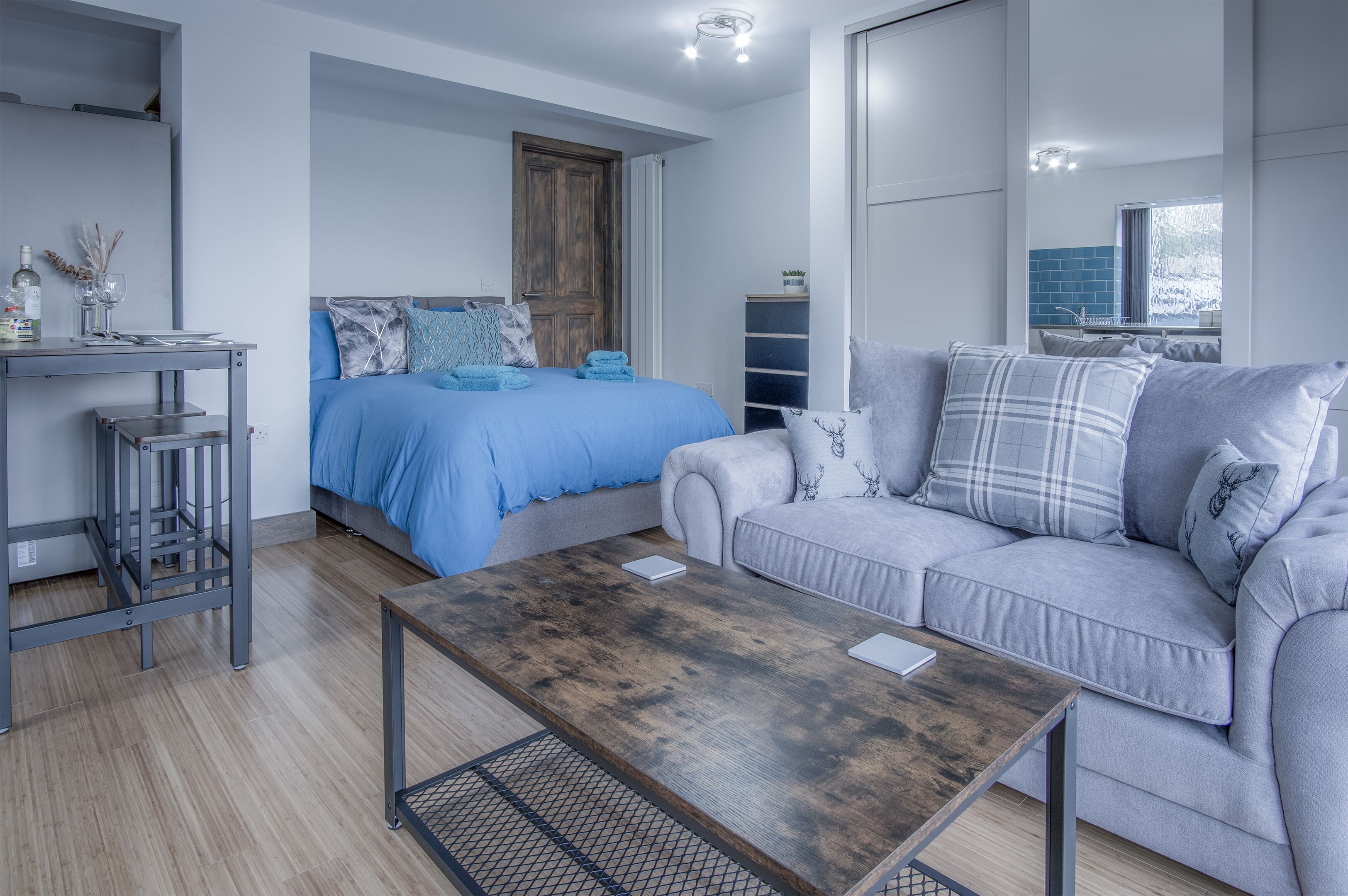 Un dormitorio moderno con una cama, un sofá gris, una mesa de centro de madera y un escritorio pequeño con una silla.