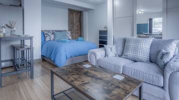 Un dormitorio moderno con una cama, un sofá gris, una mesa de centro de madera y un escritorio pequeño con una silla.