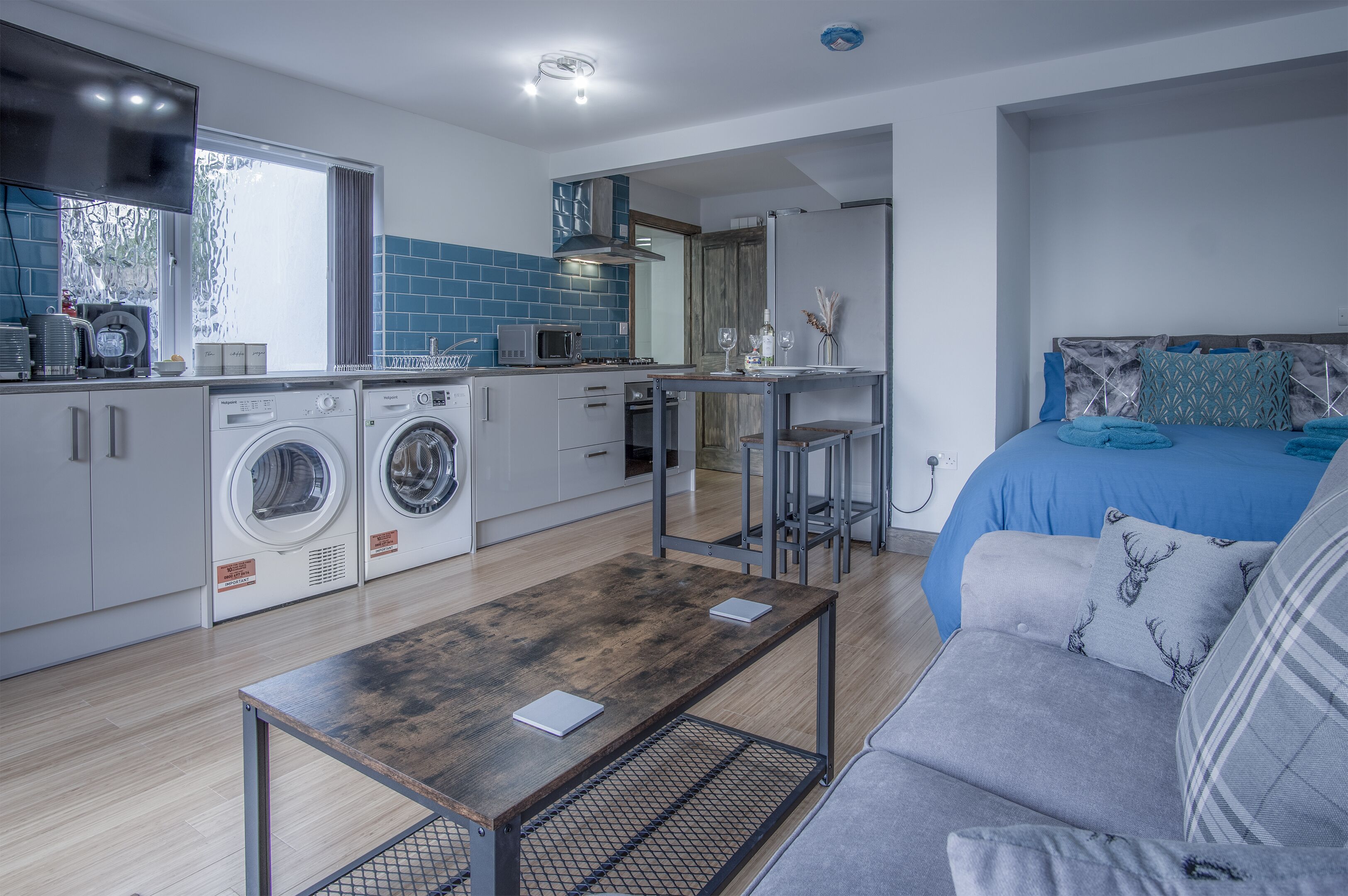 A compact living space with a kitchenette, a washing machine, a dining table, and a bed.