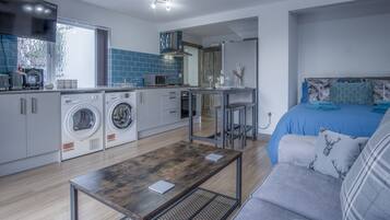 A compact living space with a kitchenette, a washing machine, a dining table, and a bed.