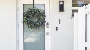 Une porte blanche avec un panneau en verre dépoli, un interphone et une boîte aux lettres fixées au mur.