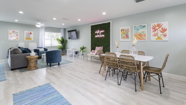 Un salon moderne avec un coin repas, comprenant un téléviseur à écran plat, un mur vert agrémenté d’un néon, et des œuvres d’art accrochées aux murs.