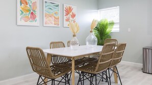 Un coin repas avec une table ronde, six chaises en osier et trois œuvres d’art encadrées accrochées au mur.
