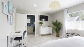 Une chambre à coucher moderne avec un lit, un bureau, une chaise, une plante en pot et un téléviseur fixé au mur.