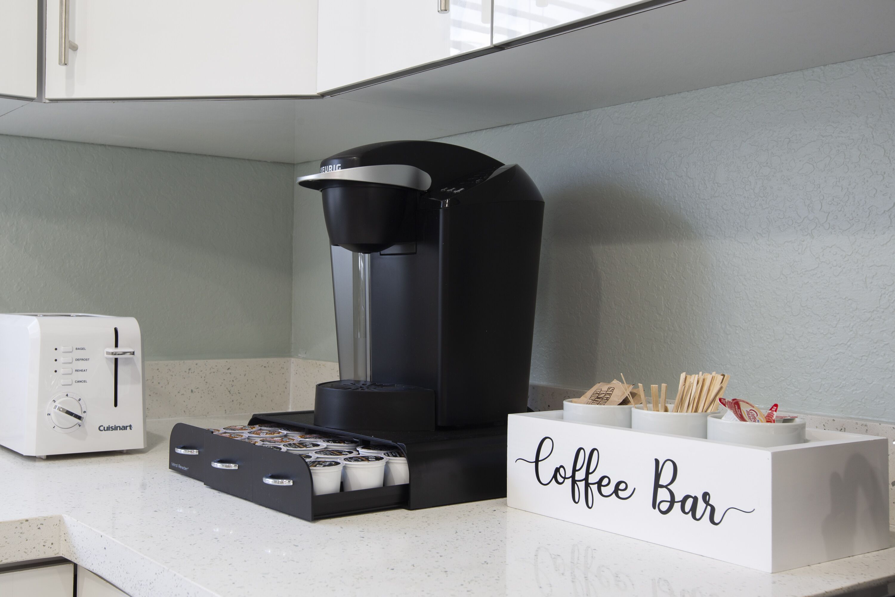 A kitchenette with a coffee maker, a toaster, and a coffee bar sign.