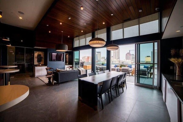 A modern interior with a dining area, kitchen, and large windows offering a city view.