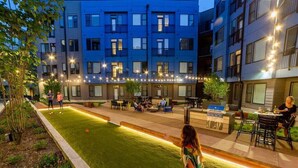 A courtyard with a grassy area, outdoor seating, and a building with multiple floors and balconies. - Downtown Indy Apartment w/ Balcony, Pool & Parking (Indianapolis)