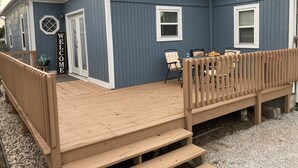 Une maison bleue avec une terrasse en bois, un panneau d’accueil et une table avec des chaises à l’extérieur.