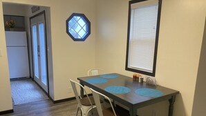 Un coin repas avec une table en bois foncé, quatre chaises blanches et des sets de table bleus.