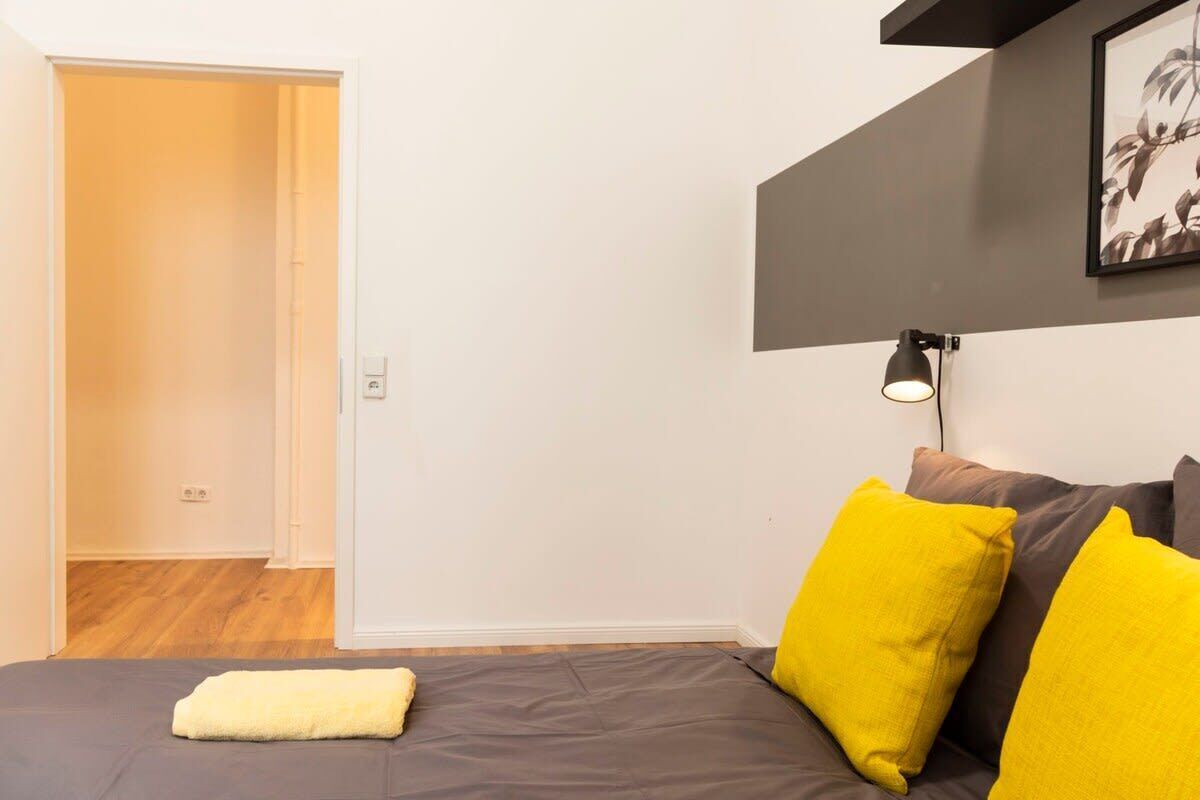 Un dormitorio con una cama, una lámpara de noche y una puerta que da a otra habitación.