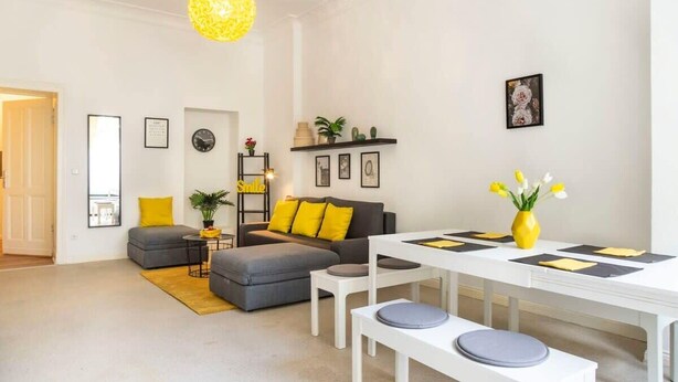 Un salon moderne avec un canapé gris, des coussins jaunes, une table à manger blanche et une suspension jaune.