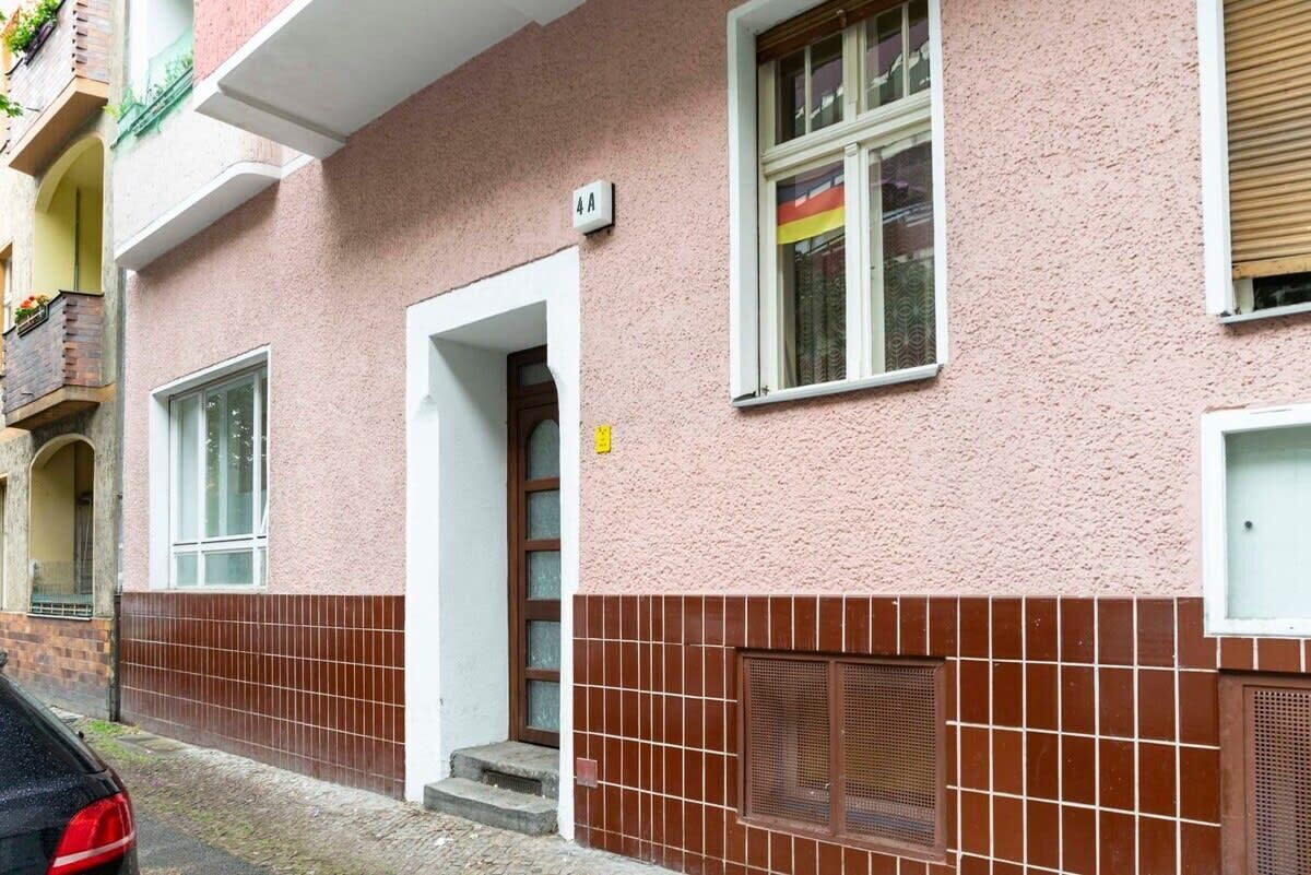 Un edificio con fachada rosa, base de ladrillo marrón, una puerta y una ventana con una bandera.