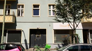 Un immeuble à plusieurs étages dont la façade est ornée d’un motif solaire central, doté de nombreux balcons et d’une devanture avec une enseigne.