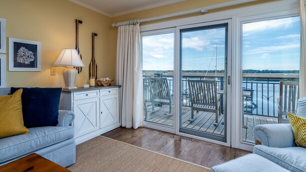 A living room with a sofa, a coffee table, a lamp, and a view of a balcony with outdoor furniture. - Waterfront living at Bohicket Marina, spacious 3BR townhome in Seabrook Island! No Pets Allowed. (Seabrook Island)