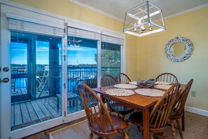 A dining area with a wooden table and chairs, a view through glass doors to an outdoor deck, and a decorative mirror on the wall.