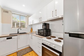 Una cocina moderna con gabinetes blancos, un refrigerador de acero inoxidable, horno empotrado y microondas.