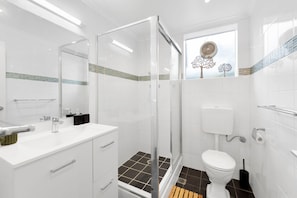 Een moderne badkamer met een douchecabine van glas, een toilet en een wastafel met spiegel.