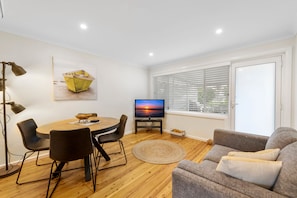 Een moderne woonkamer met een ronde eettafel, twee stoelen, een televisie en een bank.