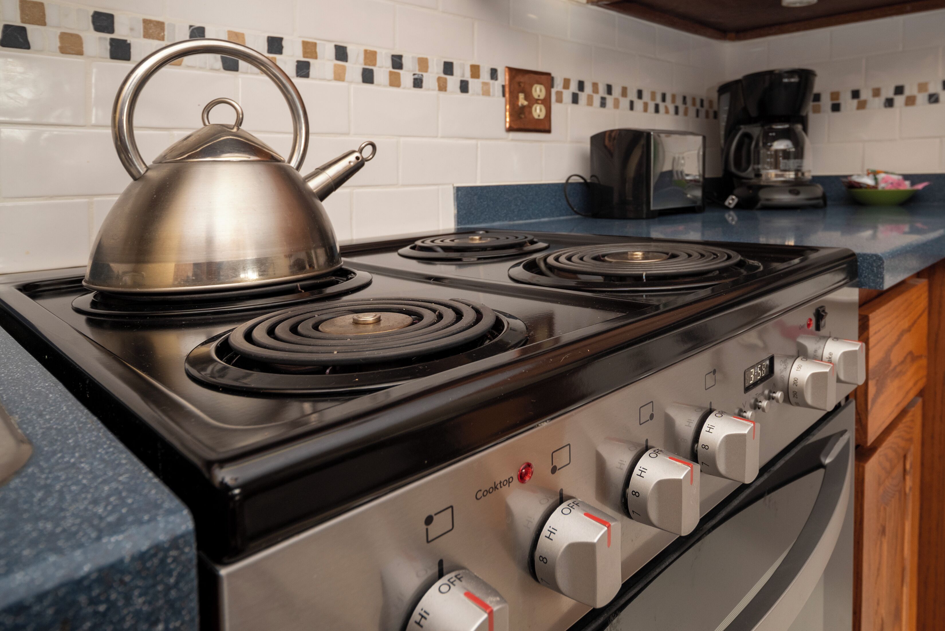 Una cocina con estufa, hervidor y cafetera.