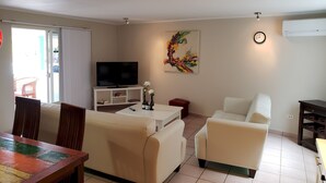 Un soggiorno con televisione, un quadro, un orologio e un'area pranzo con tavolo e sedie.