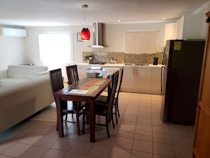 A modern kitchen with a dining table, chairs, a sofa, and a refrigerator.