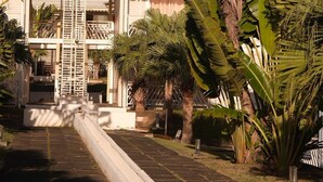 A building with a white facade, a central staircase, and surrounding palm trees. - Cozy single bedroom apartment with pool and private beach (Saint-François)