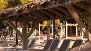 A beachside area with wooden pergolas, white lounge chairs, and a sign for 'Manny's Restaurant'. - Cozy single bedroom apartment with pool and private beach (Saint-François)