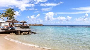 A beach with clear turquoise water, palm trees, and a wooden pier with lounge chairs. - Cozy single bedroom apartment with pool and private beach (Saint-François)