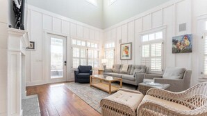 A spacious living room with a wooden floor, a grey sofa, a black armchair, a wicker sofa, and a coffee table. - Walk-to-Beach Luxury Coastal Home Near Pier Village, St. Simons Island (St. Simons Island)