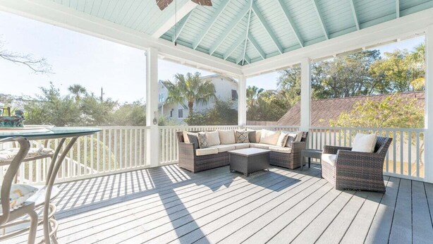 A covered outdoor deck with wicker furniture and a table. - Walk-to-Beach Luxury Coastal Home Near Pier Village, St. Simons Island (St. Simons Island)