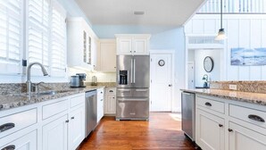 A modern kitchen with white cabinetry, stainless steel appliances, and a wooden floor. - Walk-to-Beach Luxury Coastal Home Near Pier Village, St. Simons Island (St. Simons Island)