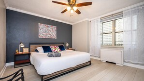 A bedroom with a bed, nightstands, a ceiling fan, a window with curtains, and a wall art piece. - Downtown Atlanta Condo with Spectacular Views (Atlanta)