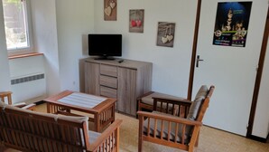 A room with a wooden table and chairs, a television on a cabinet, and a window with blinds.
