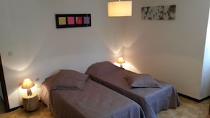 A room with two single beds, each with a lamp. There is a wall-mounted artwork above the beds and a small table with a lamp beside one of the beds.