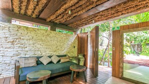 A wooden deck with a stone wall, a green sofa with cushions, and a small round table. - Eco-Lifestyle Community with Magnificent Amenities  (Tulum)