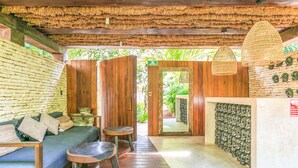 A wooden interior with a sofa, two stools, a woven ceiling, and a wall of carved masks. - Eco-Lifestyle Community with Magnificent Amenities  (Tulum)