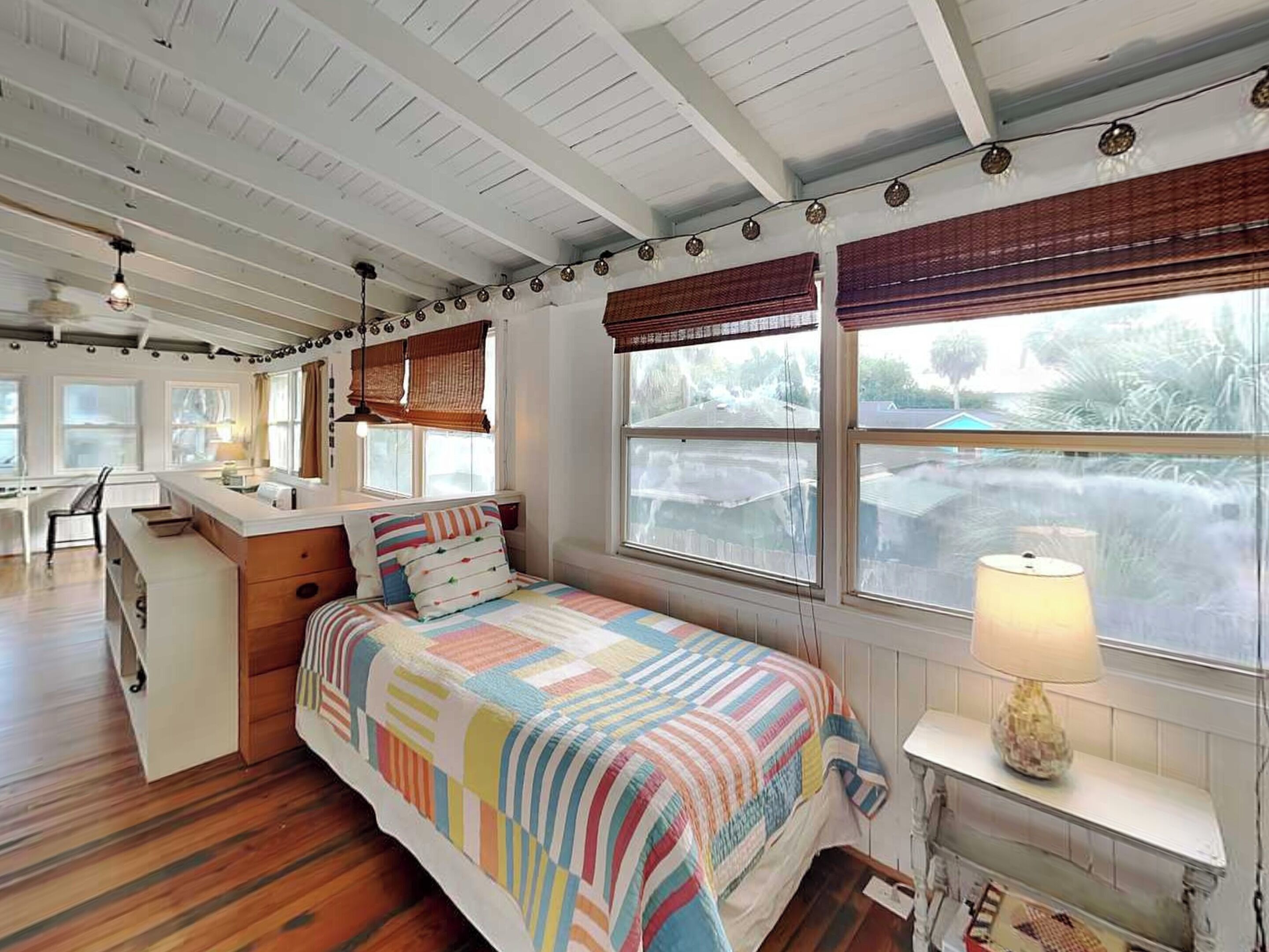 A bedroom with a bed, a desk, and a window with blinds.