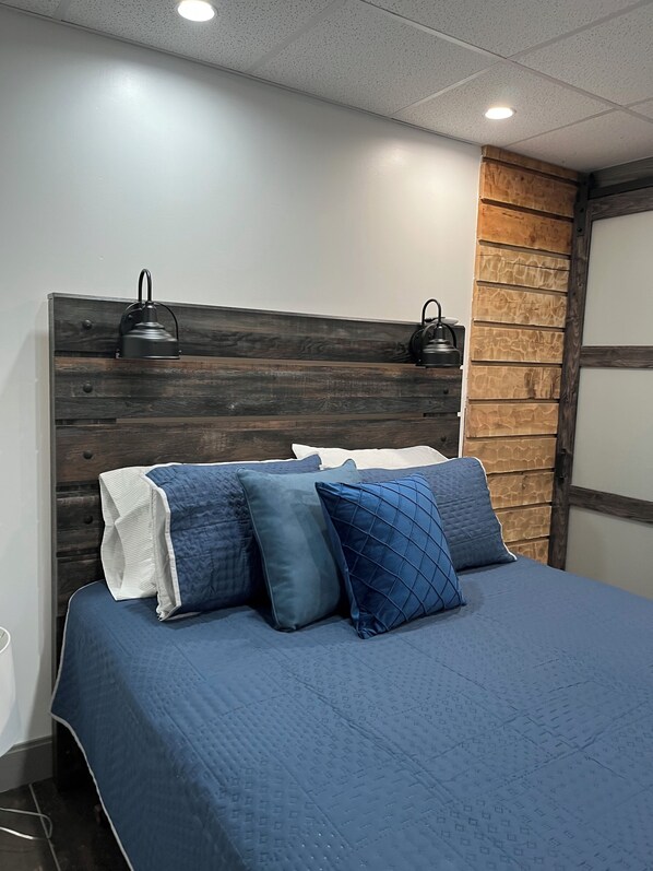 Un letto con una coperta e dei cuscini blu scuro, una testiera in legno e due lampade fissate al muro.