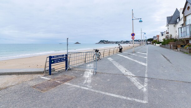 Een kustweg met een strand, een bord dat een toeristenbureau aangeeft, en een fiets bij de reling.