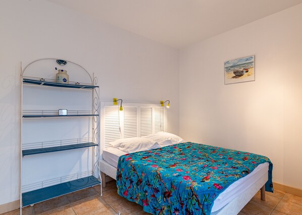 A bedroom with a bed, a shelf unit, a headboard with lights, and a painting on the wall. - Les Voiles - appartement avec terrasse - plage à 50 m (Pléneuf-Val-André)