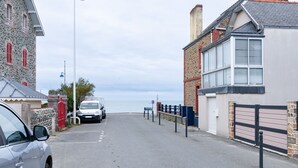 Een kuststraat met een stenen gebouw, een geparkeerde auto en uitzicht op zee.