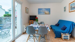 Een eetgedeelte met een tafel voor twee personen, een blauwe bank en een televisie op de achtergrond.