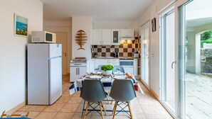 Een compacte keuken met een koelkast, magnetron en een zwart-wit geruit spatwand. Er is een eettafel met stoelen en een potplant.