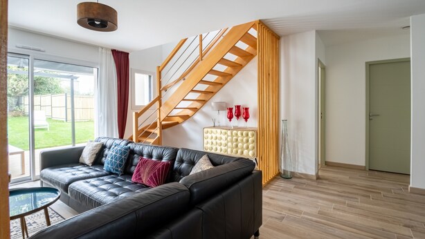 Una sala de estar moderna con un sofá de cuero negro, una mesa de centro de vidrio y una escalera de madera.