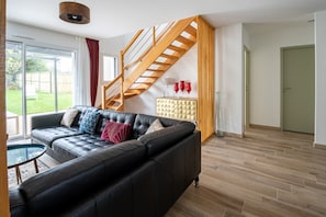 A modern living room with a black leather sofa, a glass coffee table, and a wooden staircase.