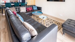 Una sala de estar moderna con un sofá de cuero negro, una mesa de centro de vidrio y un tapete estampado.